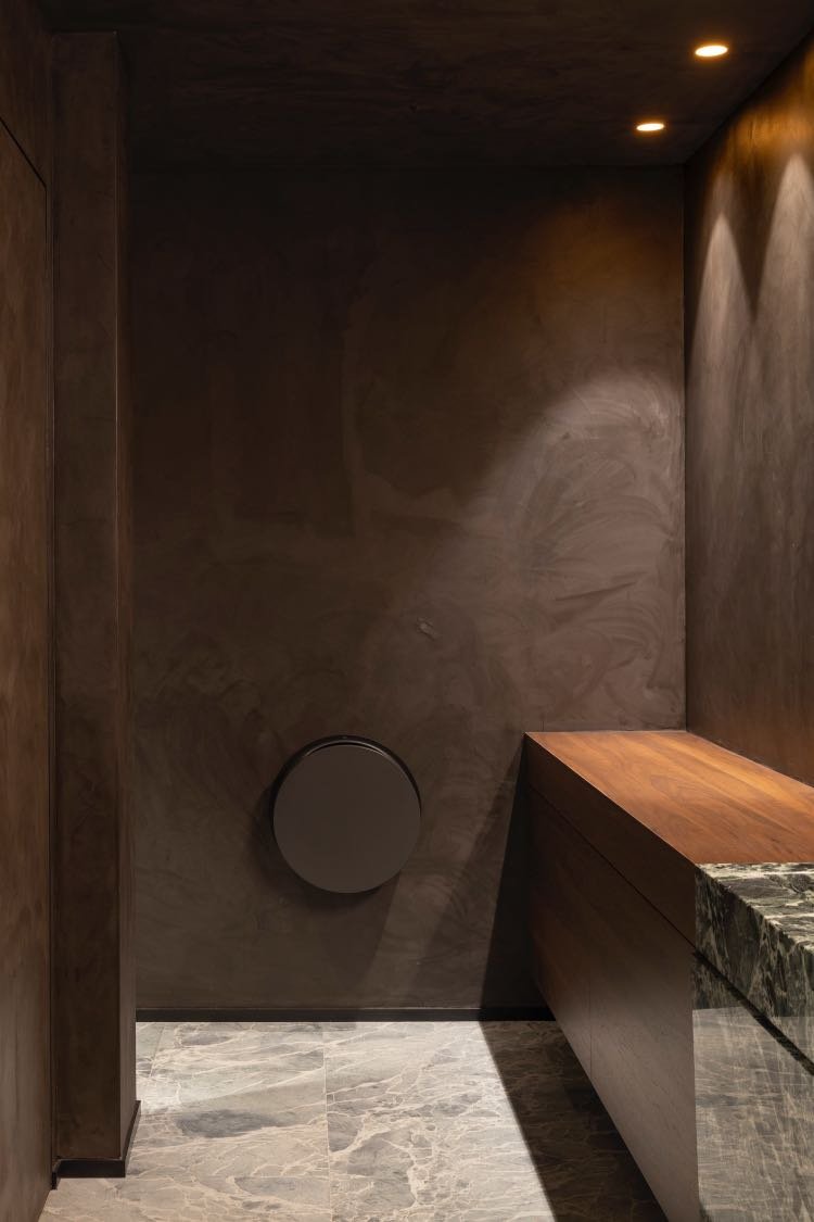 Baño minimalista con paredes y techo de microcemento oscuro, iluminación empotrada y encimera de madera.